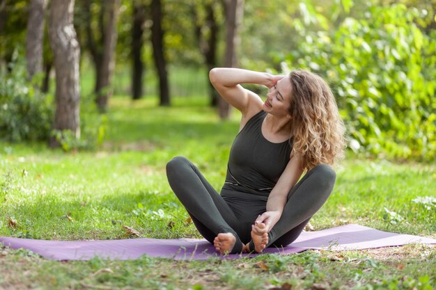 Happy Caucasian yogi woman sitting on a mat on the grass Healthy lifestyle