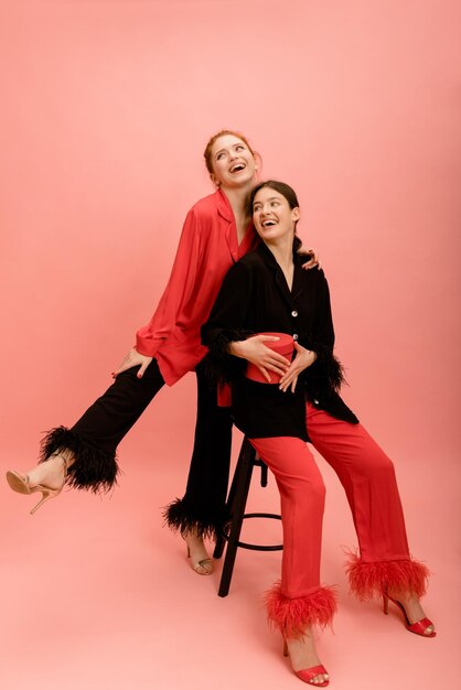 Happy caucasian young ladies brunette and redhead in colorful clothes look away on pink background Modern lifestyle concept