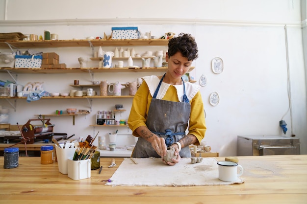 Foto felice ragazza ceramista in laboratorio studio preparare argilla grezza per la modellazione alle lezioni artigianale hobby