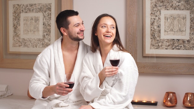Счастливая очаровательная пара пьет вино и смеется в современном оздоровительном салоне