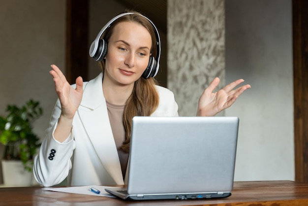 A happy charming young business woman wearing a headset is having a video call on laptop Young woman in office