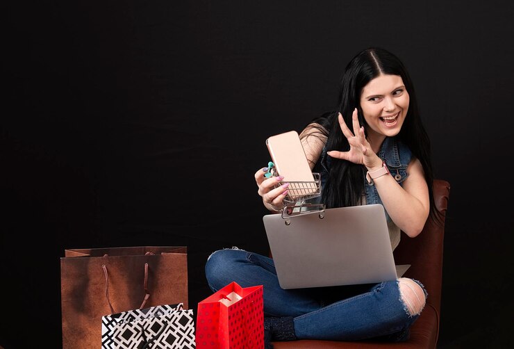 फोटो happy charming young woman with shopping cart and smartphone using laptop for shopping online