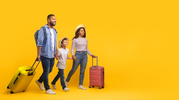 Happy cheerful african american family of three walking with suitcases