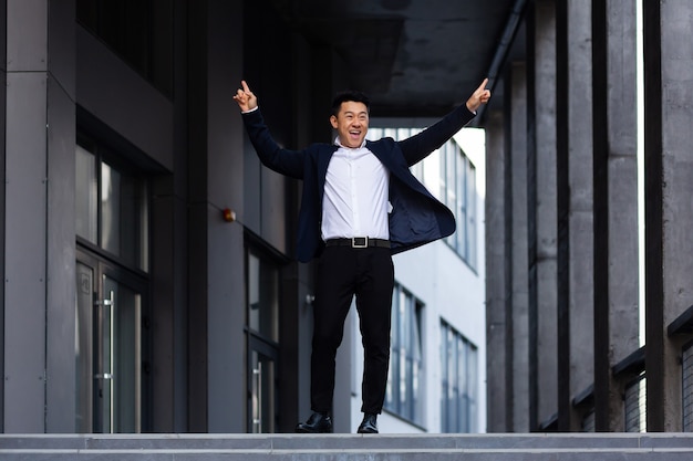 Happy and cheerful Asian businessman dancing near the office rejoices in victory and success