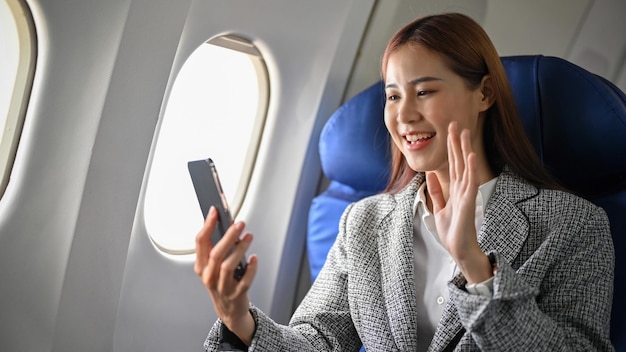 Счастливая и веселая азиатская деловая женщина, использующая смартфон во время полета