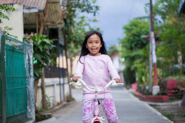 自転車に乗って幸せな陽気なアジアの子供の女の子