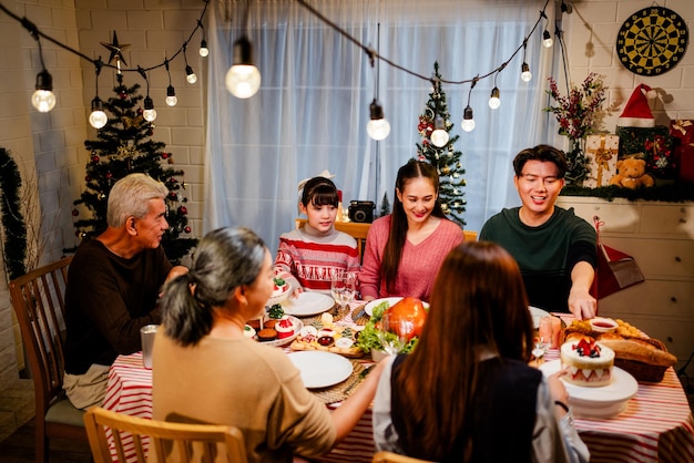 幸せで陽気なアジアの家族は ⁇ 家でクリスマスディナーで話し合い ⁇ 笑顔で休日を祝います ⁇ 