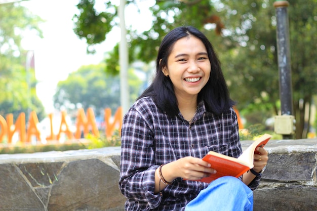 happy cheerful asian female student reading a book and laughing enjoying vacation