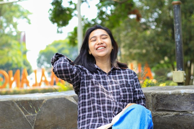 happy cheerful asian female student reading a book and laughing enjoying vacation