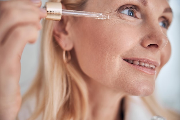 Happy cheerful blonde Caucasian female taking skin facial care in the morning