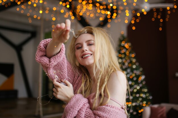 Photo happy cheerful blonde woman celebrates new year by the christmas tree