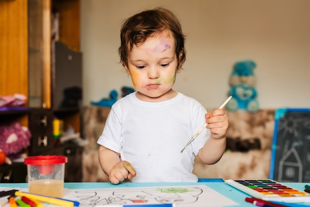 Happy cheerful child drawing with brush in album using a lot of painting tools.