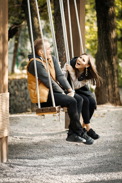 Happy cheerful couple closeup in autumn in the park in the forest in the afternoon on a wooden swing