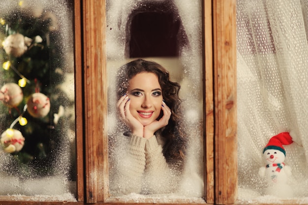Foto felice ragazza allegra guardando attraverso la finestra congelata