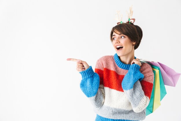 Happy cheerful girl wearing sweater standing isolated on white, carrying shopping bags