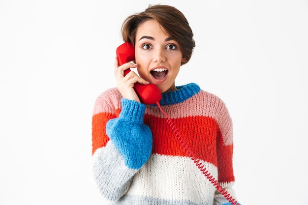 白で隔離のセーターを着て、固定電話で話している幸せな陽気な女の子