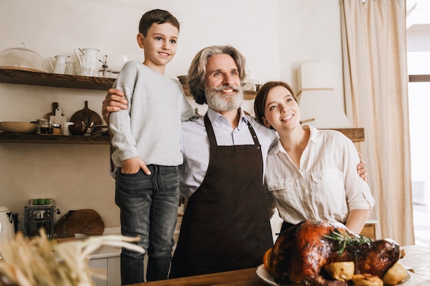 Счастливый веселый дедушка стоит на кухне с дочерью и внуком, празднует