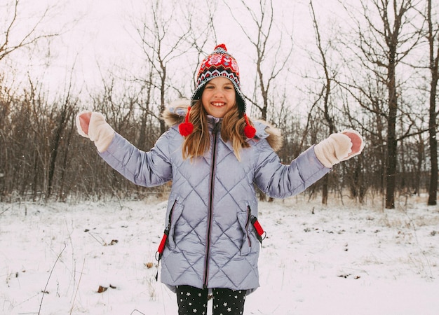 Happy cheerful little girl having fun in the forest on a winter day. child plays with snow.