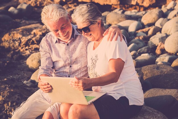 Happy cheerful modern couple of senior caucasian people together using a technoogy laptop computer outdoor with internet connection