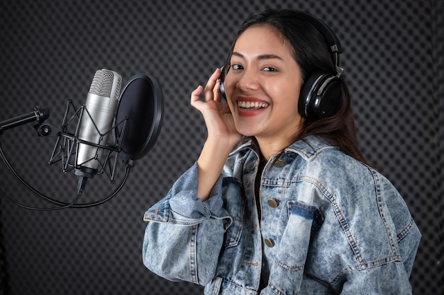 Felice allegro piuttosto sorridente del ritratto di una giovane cantante asiatica che indossa le cuffie che registra una canzone davanti al microfono in uno studio professionale