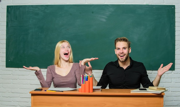 Happy and cheerful pretty teacher and handsome schoolmaster\
smiling at desk university or college students high school\
education couple studying in classroom man and woman back to\
school