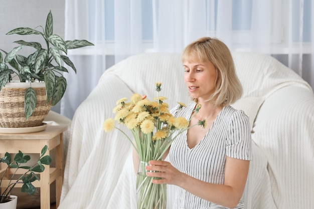 Felice, allegra, sorridente donna matura di mezza età in soggiorno, con un mazzo di fiori gialli.