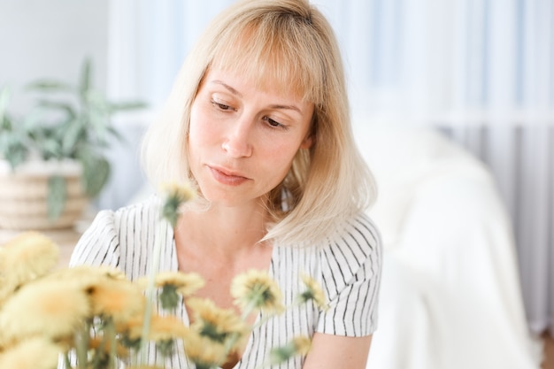 黄色い花の花束と、リビングルームで幸せな、陽気な、笑顔の中年女性。