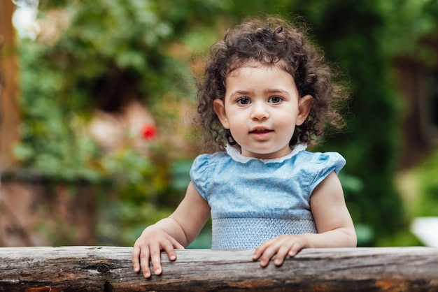 写真 木製のフェンスに寄りかかってカメラを見つめる巻きの幸せな幼児の女の子