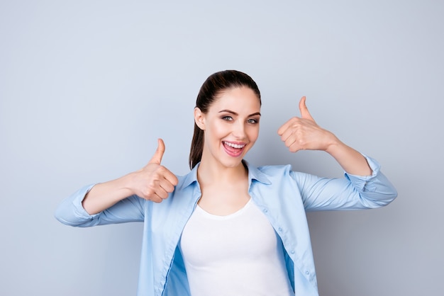 Happy cheerful woman in blue shirt showing thumbs up  isolated gray space