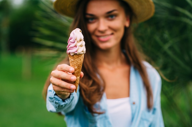 La donna allegra felice in camicia e cappello gode del gelato alla frutta dolce all'aperto nel giorno di estate caldo