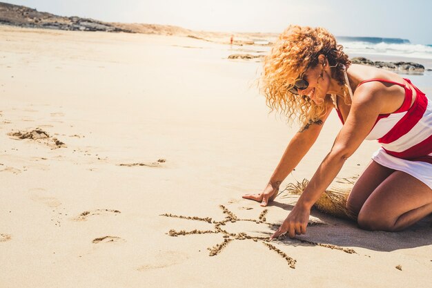 Happy cheerful woman on summer vacation enjoying the beach and the outdoor designing a sun on the sand 