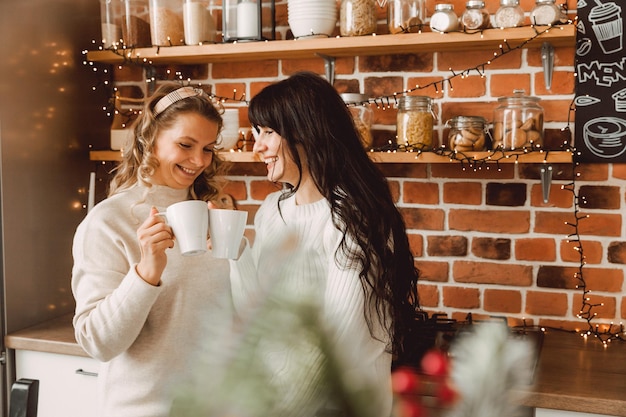 Happy and cheerful women talking and drinking coffee at home in the kitchen. blonde and brunette talking to each other