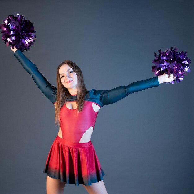 Happy cheerleader girl in uniform dancing with pompoms isolated on grey background