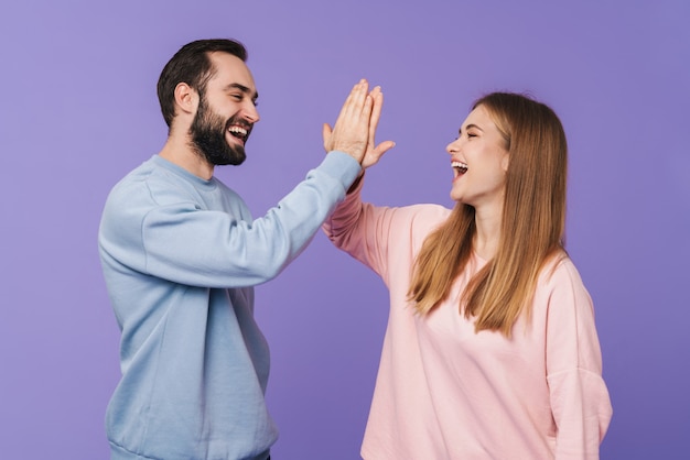 happy cheery optimistic loving couple posing isolated over purple wall giving high five.