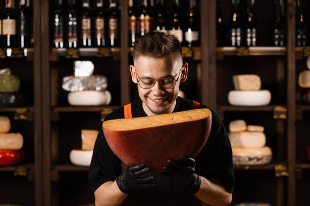 Happy cheese sommelier holding limited gouda cheese and smile Creative worker of cheese shop Snack tasty piece of cheese for appetizer