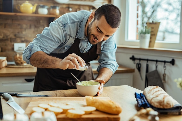 Chef felice che prepara il condimento al guacamole e lo condisce con sale mentre prepara il cibo in cucina