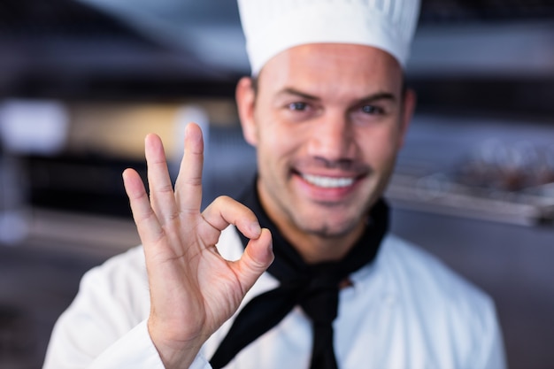 Счастливый шеф-повар делает знак ОК в коммерческой кухне