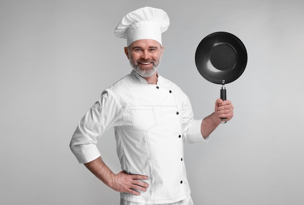 happy chef in uniform holding wok on grey background