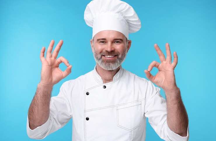 Photo happy chef in uniform showing ok gesture on light blue background