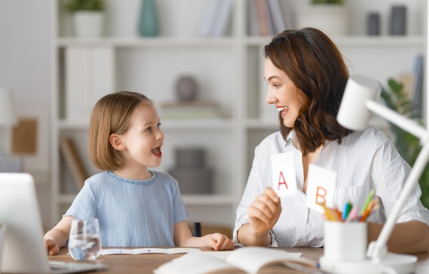 Happy child and adult are sitting at desk Girl doing homework or online education