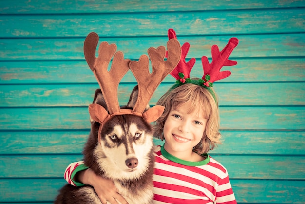クリスマスイブの子供と犬の幸せな子供とサンタクロースの帽子の赤ちゃんに身を包んだペットがhを楽しんでいます