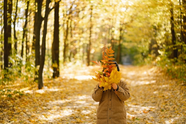 Bambino felice bambino che ride e gioca nel giorno d'autunno, il bambino si copre il viso con le foglie