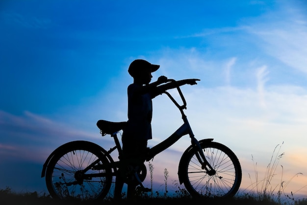 Un bambino felice e un concetto di bici nella silhouette del parco all'aperto