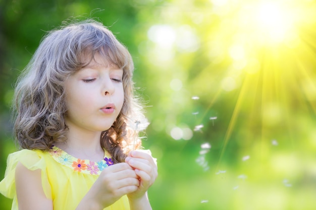 春の公園で楽しんでタンポポの花屋外の女の子を吹いて幸せな子