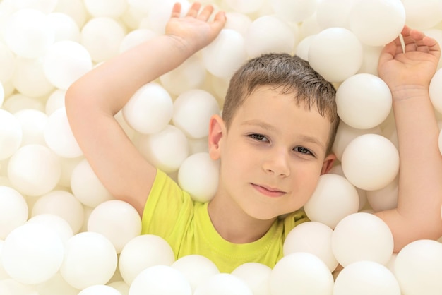 Счастливый мальчик в большом сухом бассейне с тысячей белых шариков крупным планом
