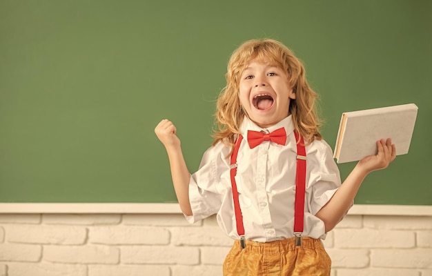 Happy child boy in bow tie study in school classrrom with\
notebook having fun copy space education