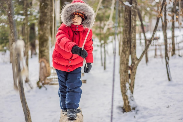 Happy child boy enjoying activity in a climbing adventure park on a winter day