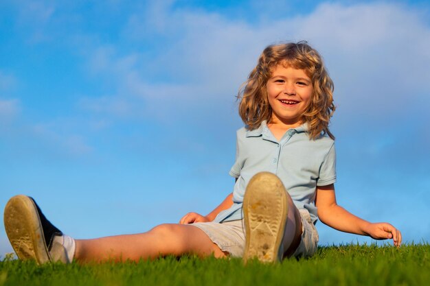 Happy child boy sitting on green grass outdoors in summer park.