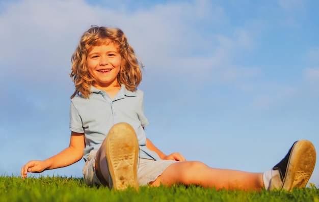 Happy child boy sitting on green grass outdoors in summer park