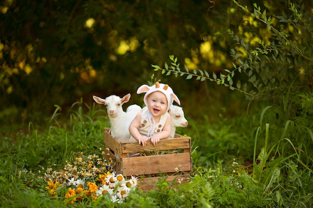 Happy child boy with white goats in spring on nature in the village with greenery and flowers.